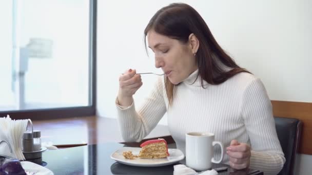 若い女性がコーヒーを飲むし、カフェでケーキを食べる — ストック動画