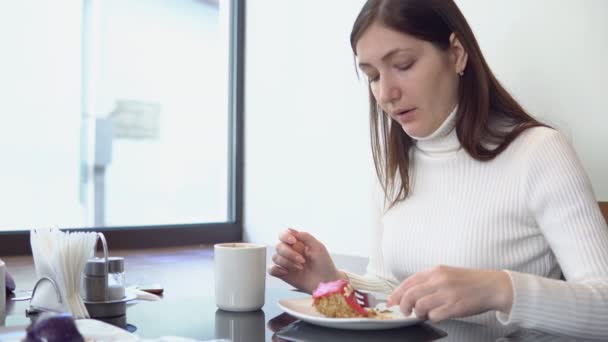 Schöne Frau am Cafétisch, Kuchen isst und Kaffee trinkt — Stockvideo