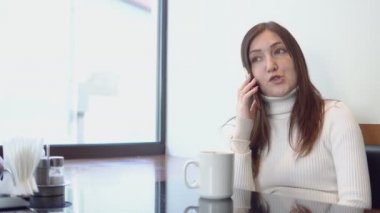 Genç güzel kadın telefonda konuşurken bir kafeterya masada oturur