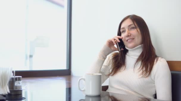 Mooie vrouw zitten op een café tafel, praten over de telefoon — Stockvideo