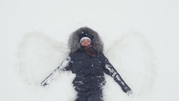 Šťastná dívka leží na sněhu a ukazuje anděl — Stock video