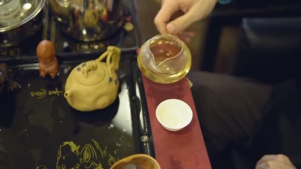 Чайная церемония Мастер наливает зеленый чай из стеклянного чайника в белую кружку — стоковое видео