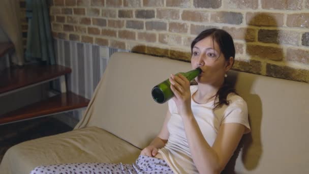 Mujer joven en el sofá delante de la televisión bebiendo cerveza — Vídeo de stock