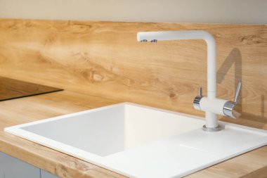 Modern beyaz kare lavabo, yumuşak ahşap mutfak yüzeyine yerleştirilmiş uzun musluk.