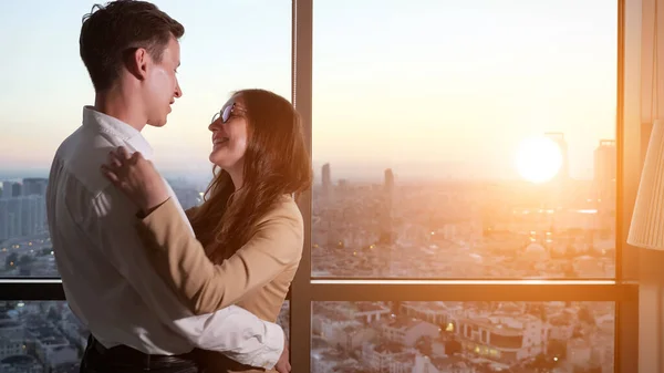 Couple, man and woman are dancing near the panoramic window with city view.
