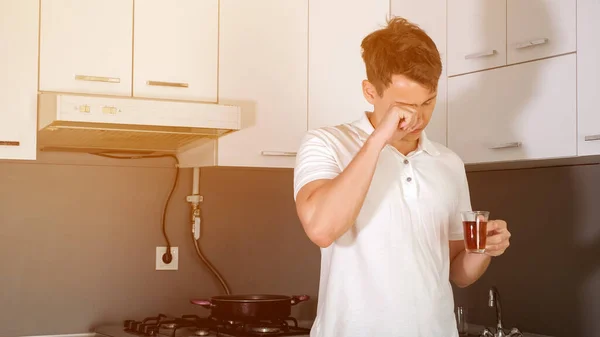 El joven soñoliento está tomando un té por la mañana en la cocina de su casa. . — Foto de Stock