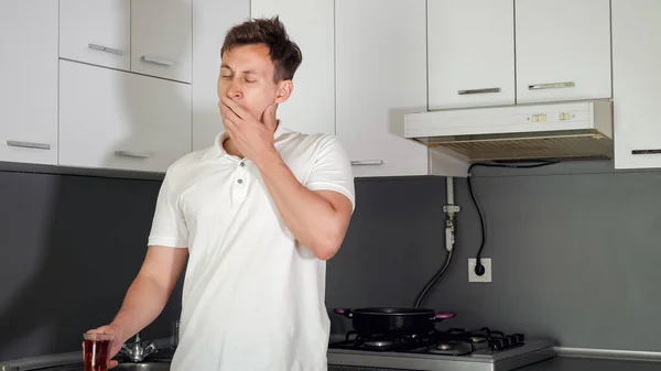 El joven soñoliento está tomando un té por la mañana en la cocina de su casa. . — Foto de Stock