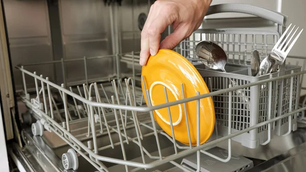 Homem coloca um prato sujo e talheres na máquina de lavar louça — Fotografia de Stock
