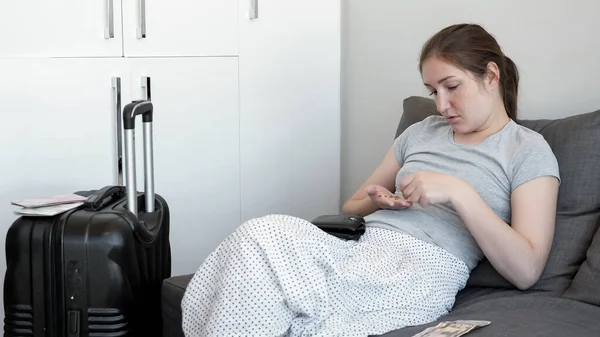 Single woman is counting her money in hotel room sitting on sofa with suitcase. — Stock Photo, Image