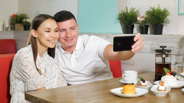 Счастливая пара делает селфи сидя за обслуживаемым столом в кафе — стоковое фото