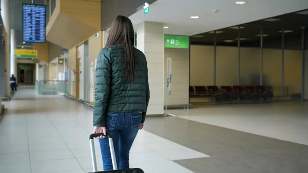 La donna viaggiatrice sta camminando nel moderno terminal dell'aeroporto portando la valigia, vista posteriore . — Foto Stock