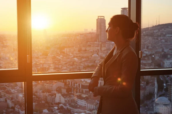 Jeune femme d'affaires au bureau debout près de la fenêtre avec vue panoramique sur la ville . — Photo