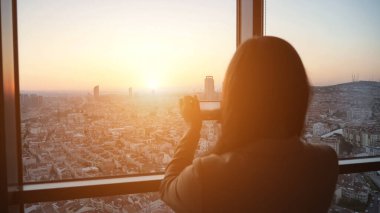 Kadın gökdelen onu modern düz akıllı telefonda gün batımında panoramik şehir görünümü fotoğrafları çeker.