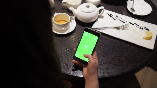 Meisjes hand bladert door de sensor van de telefoon met een groen scherm in het café. Het uitzicht vanaf de achterkant — Stockvideo