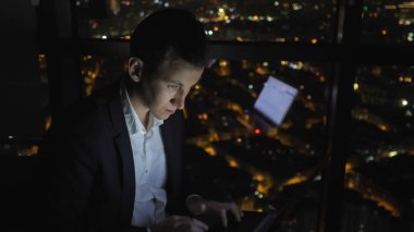 Genç adam serbest gece evde pencerenin yanında onun bilgisayar üzerinde çalışıyor.