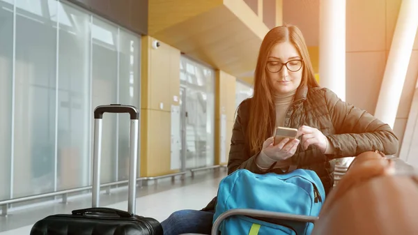 Молодая женщина проходит электронную регистрацию в смартфоне, ожидая свой рейс в аэропорту . — стоковое фото