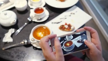Kadın bir kafede telefonla yemek fotoğrafı çekiyor.