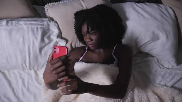 Serieuze zwarte dame kijkt naar moderne rode smartphone en types — Stockvideo
