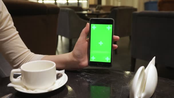 Meisjes hand holding telefoon met groen scherm in cafe — Stockvideo