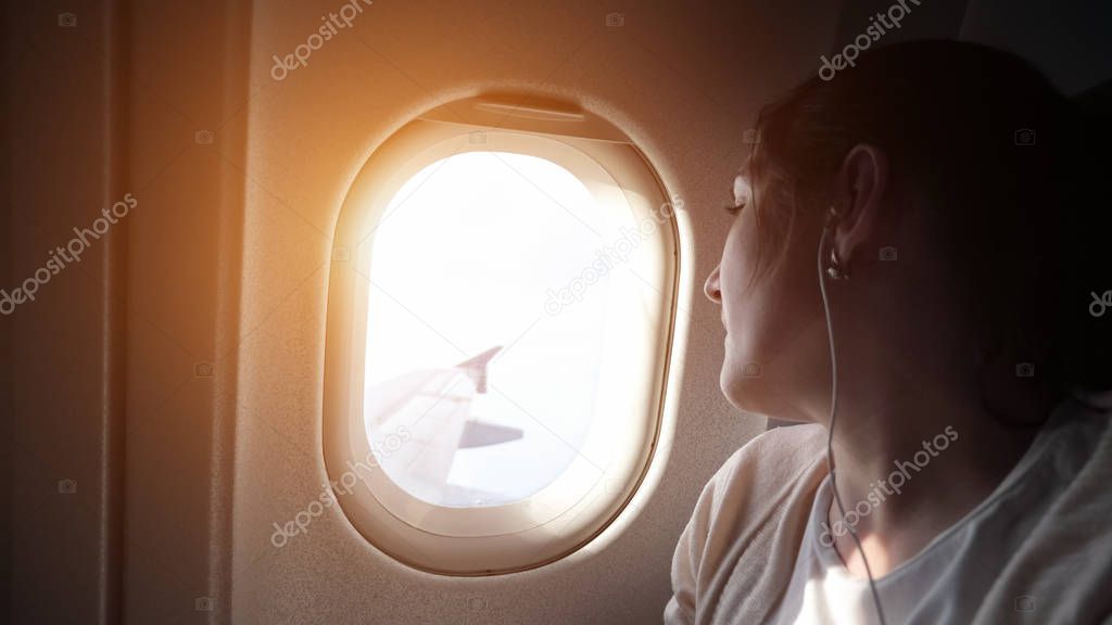 Portrait of young woman is looking at plane window.