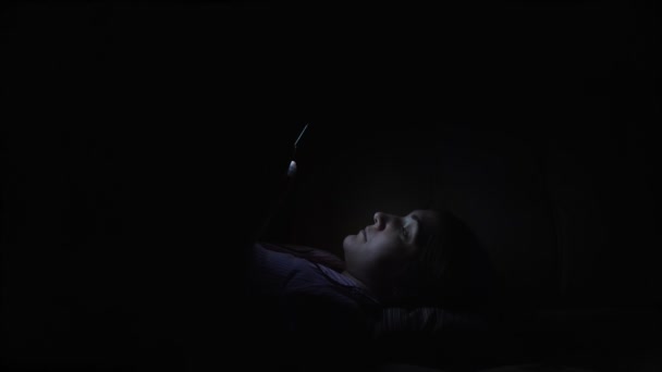 Young woman flips through social media channels on her phone in the dark — Stock Video