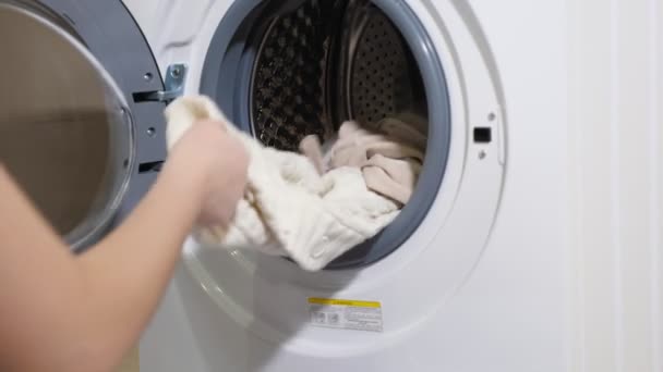 Длинноволосая девушка в футболке берет чистое белье из современной стиральной машины — стоковое видео