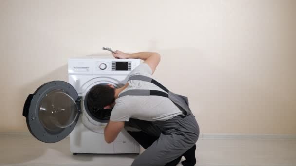Serviceman reparaties gebroken wasmachine in de buurt beige muur — Stockvideo