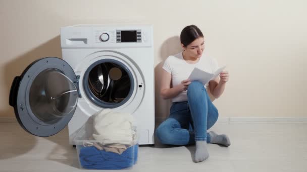 Menina lê instruções para máquina de lavar roupa perto da parede bege — Vídeo de Stock