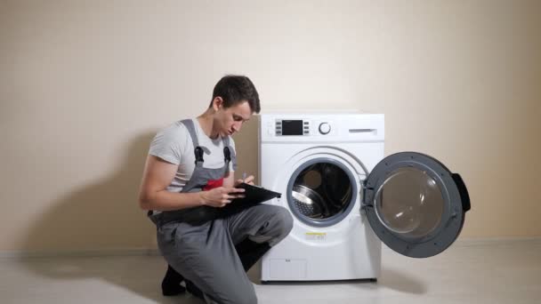Работник проверяет сломанную стиральную машину и делает заметки в комнате — стоковое видео