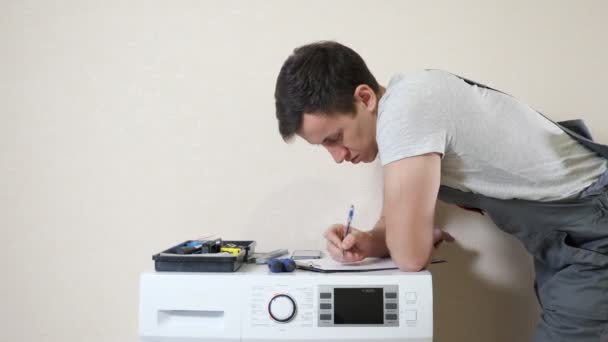 Мужчина пишет на буфер обмена, рассматривая современную стиральную машину — стоковое видео
