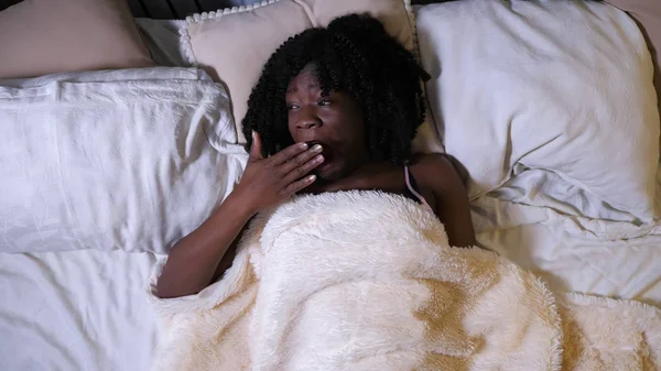 Somnoliento joven negro mujer bosteza acostado en cama queen-size —  Fotos de Stock