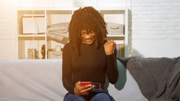 Chica afroamericana mira el teléfono inteligente y se convierte en feliz —  Fotos de Stock