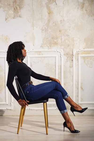 exciting black lady in blue jeans sits on brown wooden chair