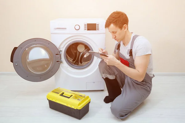 Arbeiter überprüft kaputte Waschmaschine und macht sich Notizen im Zimmer — Stockfoto