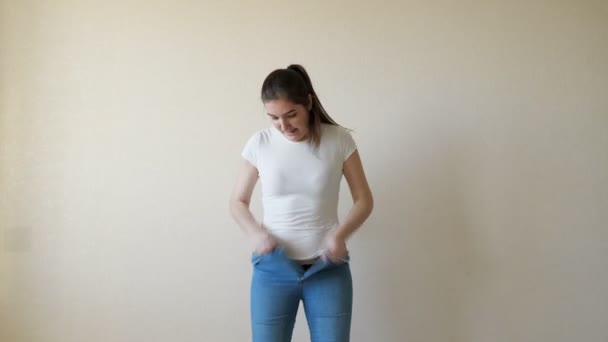 En kvinna i en vit t-hirt studsar in i sina jeans och kämpar för att knäppa dem — Stockvideo