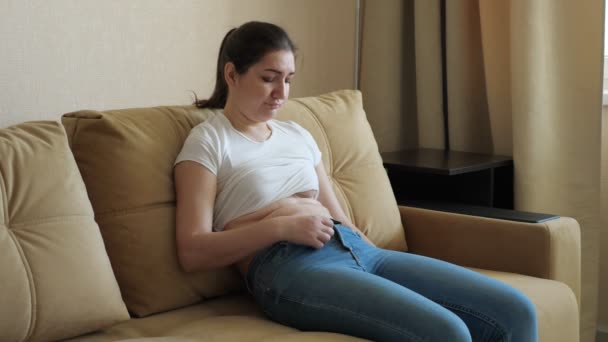 Молодая женщина сидит на диване и грустит. Избыточный вес на желудке — стоковое видео