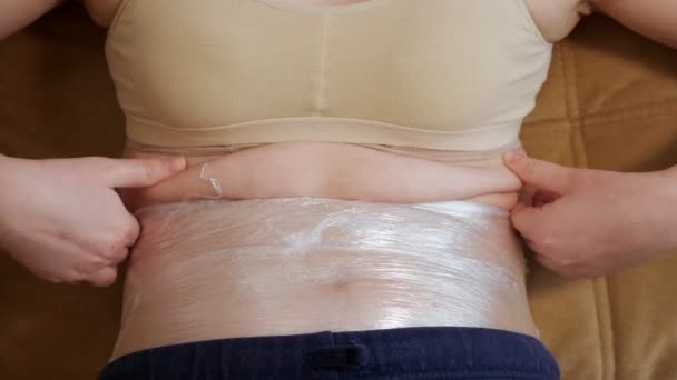 Gros plan d'un ventre de femme, qui est enveloppé dans une pellicule plastique — Video