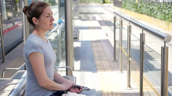 Vrouw zit op bank te wachten op tram aankomst op zonnige dag — Stockfoto