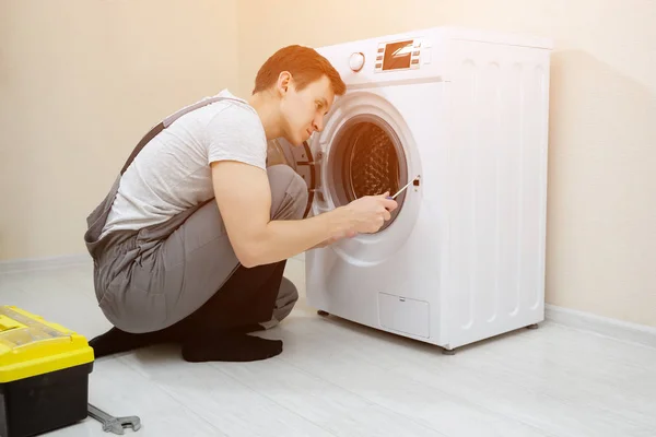 Junger Mann repariert kaputte moderne Waschmaschine auf dem Fußboden — Stockfoto