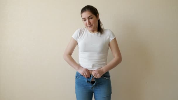 Толстая молодая женщина пытается застегнуть джинсы — стоковое видео