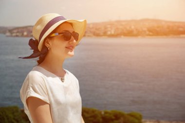 Denizin arka planında şapkalı ve gözlüklü genç kadın.