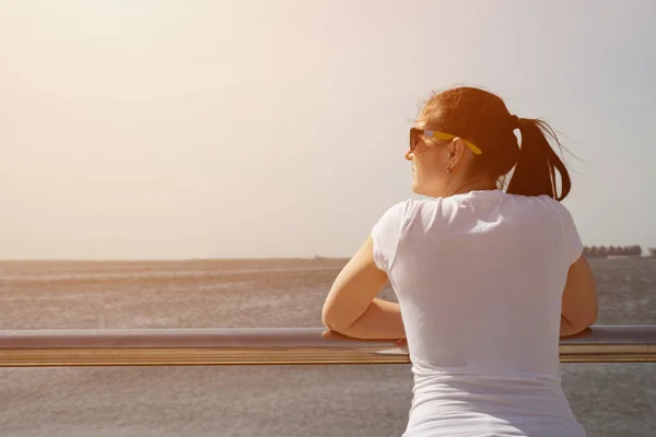 Bruneta ve slunečních brýlích se dívá na moře. — Stock fotografie