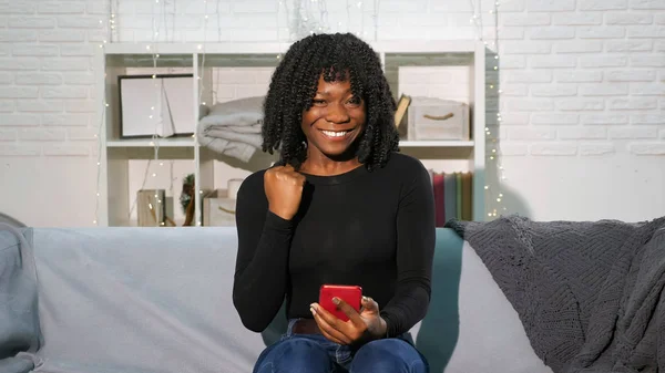 Chica afroamericana mira el teléfono inteligente y se convierte en feliz —  Fotos de Stock