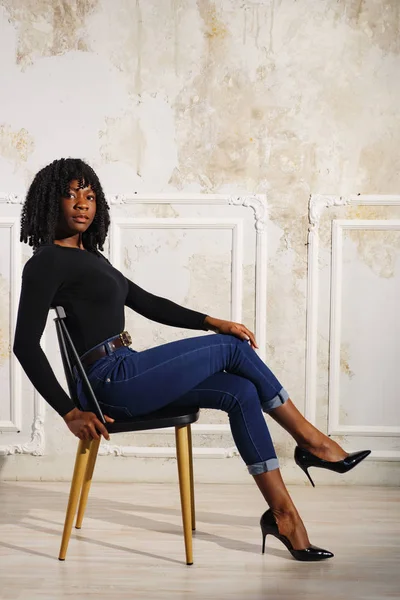 exciting black lady in blue jeans sits on brown wooden chair