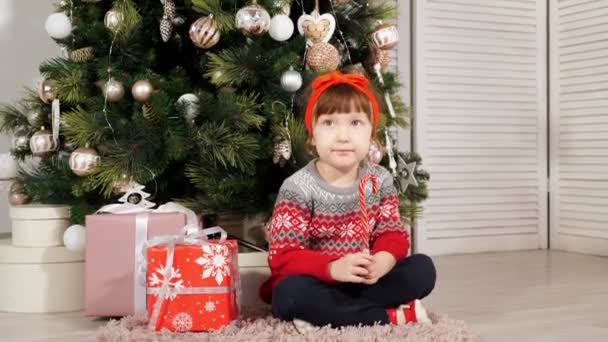小女孩坐在圣诞树下，边拍照边笑 — 图库视频影像