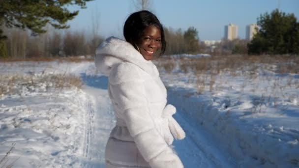 Щаслива чорна жінка йде по засніженому шляху в зимовому лісі — стокове відео