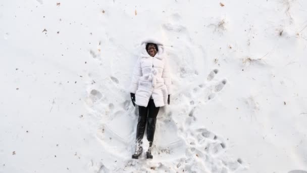 Svart flicka ligger på vit skog glänta och gör snö vinklar — Stockvideo