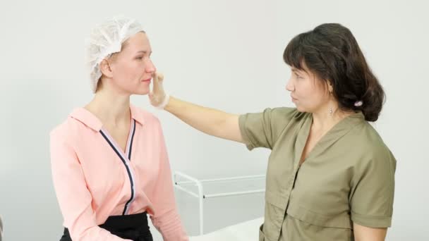 Terapeut ve sterilních rukavicích vyšetřuje pacienta na kosmetické klinice — Stock video