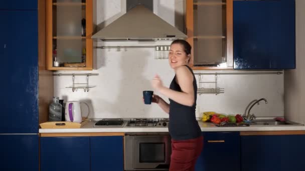 Веселая девушка танцует чашку чая и поет весело на домашней кухне — стоковое видео