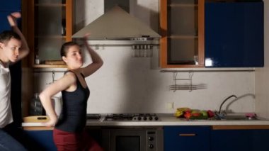 Oyuncu kız ve erkek dans edip, yüzünü buruşturup mutfakta eğleniyorlar.